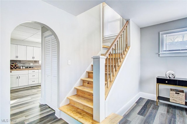 staircase with baseboards, arched walkways, and wood finished floors