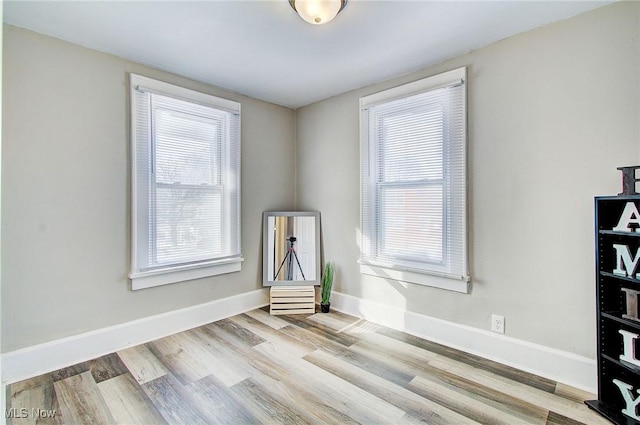 spare room featuring light wood-type flooring, a wealth of natural light, and baseboards