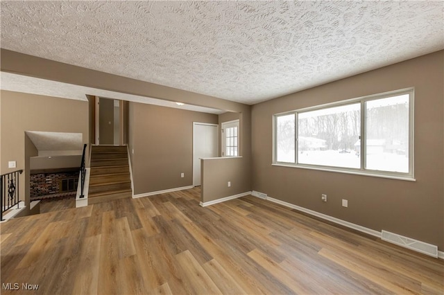 unfurnished living room featuring visible vents, light wood-style floors, a textured ceiling, baseboards, and stairs