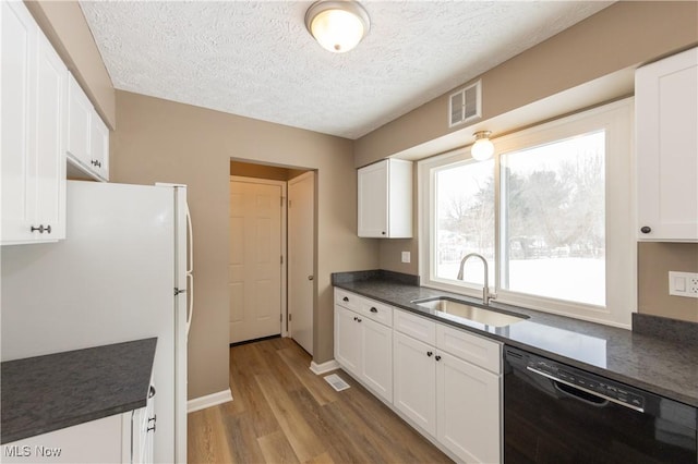 kitchen with black dishwasher, visible vents, dark countertops, white cabinetry, and a sink