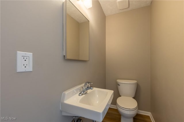 half bath with a textured ceiling, toilet, wood finished floors, a sink, and baseboards