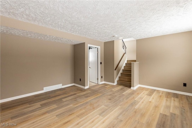 unfurnished room with baseboards, visible vents, stairway, wood finished floors, and a textured ceiling