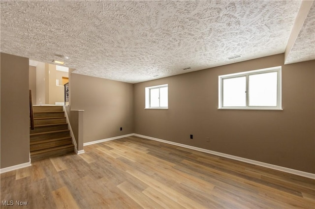 unfurnished room with visible vents, a textured ceiling, wood finished floors, baseboards, and stairs