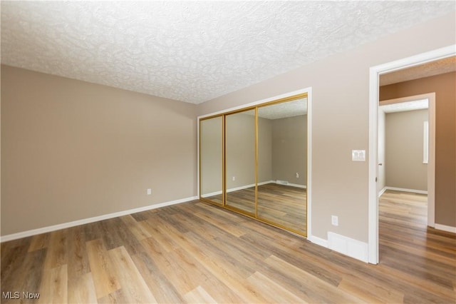 unfurnished bedroom with a textured ceiling, a closet, wood finished floors, and baseboards