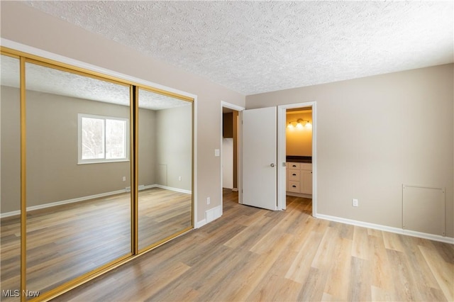 unfurnished bedroom with a textured ceiling, baseboards, a closet, light wood finished floors, and ensuite bath