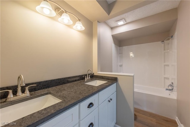 bathroom with wood finished floors, double vanity, shower / washtub combination, and a sink