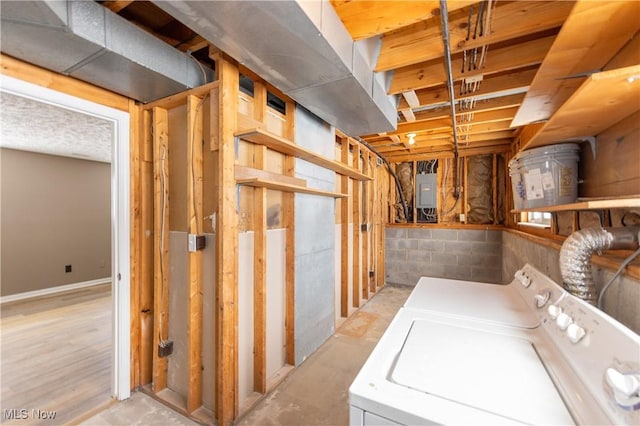 unfinished basement featuring concrete block wall, electric panel, and washing machine and clothes dryer