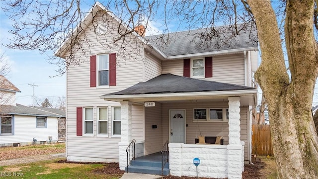 traditional home with covered porch, roof with shingles, and fence