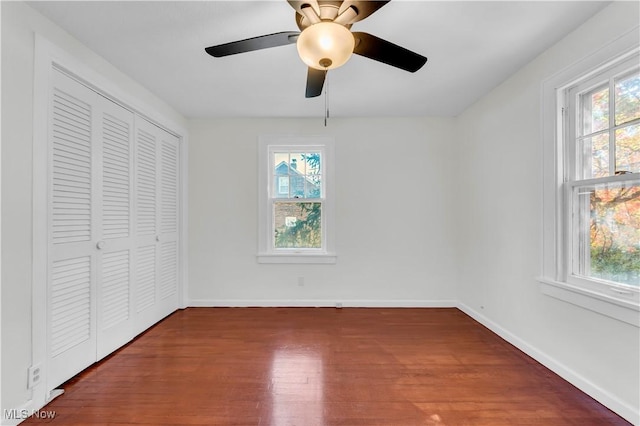 unfurnished bedroom featuring dark wood-style floors, multiple windows, baseboards, and a closet