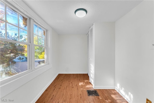 empty room featuring light wood-style flooring, visible vents, and baseboards