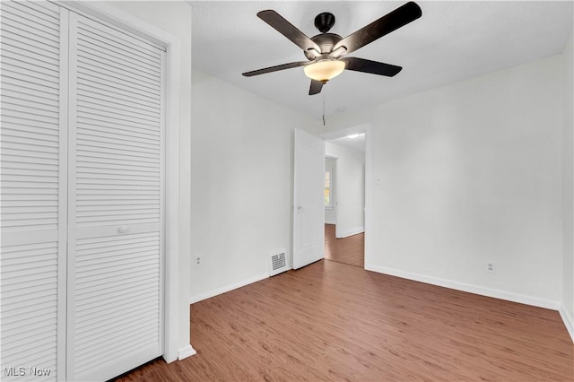 unfurnished bedroom featuring ceiling fan, wood finished floors, visible vents, baseboards, and a closet