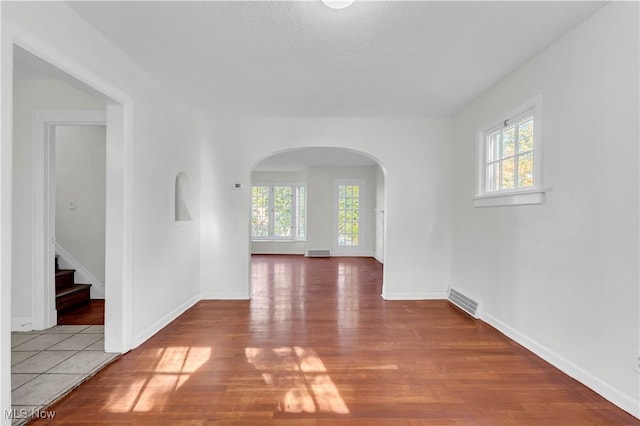 spare room featuring arched walkways, wood finished floors, visible vents, and baseboards