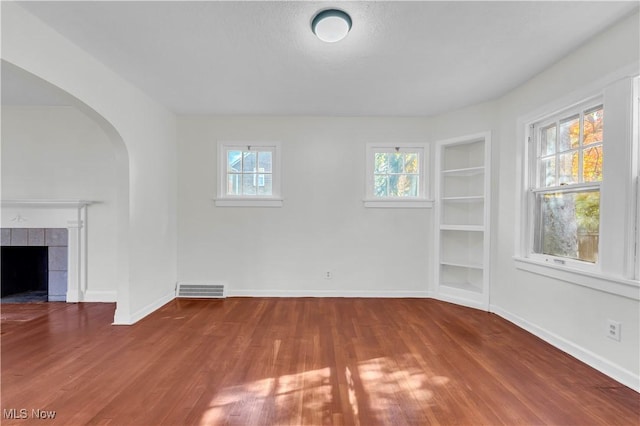 unfurnished living room featuring built in shelves, wood finished floors, and a wealth of natural light