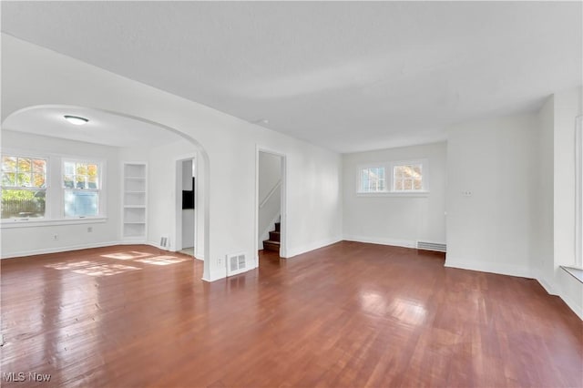 empty room featuring arched walkways, dark wood finished floors, visible vents, and built in features