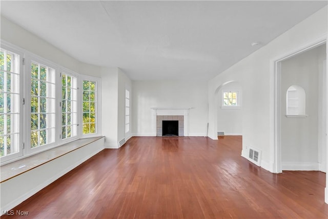 unfurnished living room featuring plenty of natural light, visible vents, dark wood finished floors, and a tiled fireplace