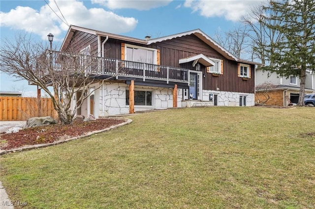 view of front of property featuring stone siding, a deck, a front lawn, and fence