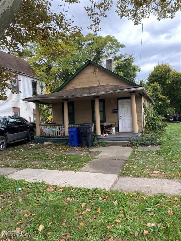 bungalow featuring covered porch, a chimney, and a front yard
