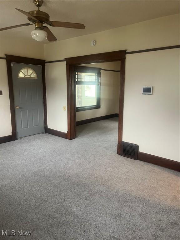 carpeted empty room featuring a ceiling fan, visible vents, and baseboards