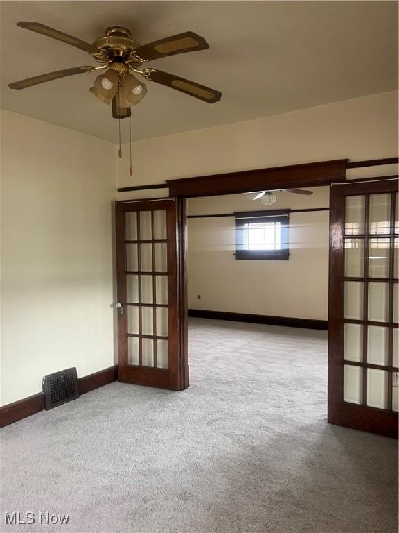 unfurnished room featuring light colored carpet, a ceiling fan, baseboards, visible vents, and french doors