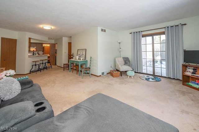 living area with baseboards, visible vents, and light colored carpet