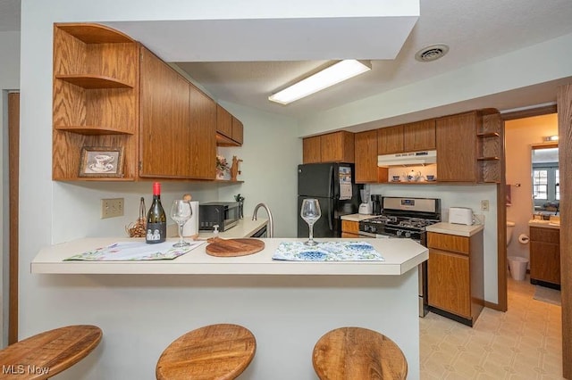 kitchen featuring freestanding refrigerator, light countertops, a peninsula, and a kitchen bar