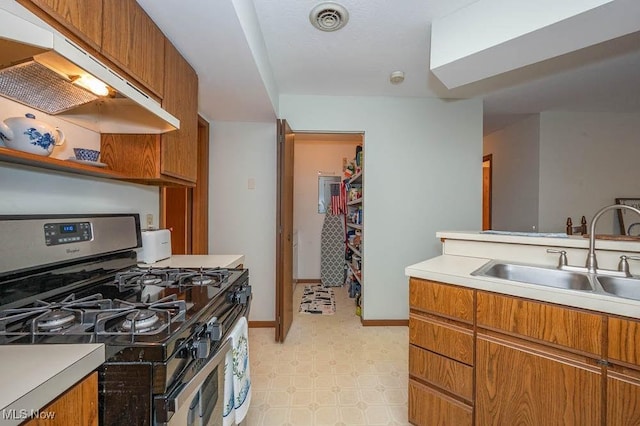 kitchen featuring light countertops, brown cabinetry, a sink, under cabinet range hood, and stainless steel gas range oven