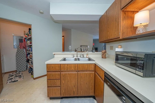 kitchen featuring a peninsula, a sink, light countertops, brown cabinetry, and stainless steel microwave