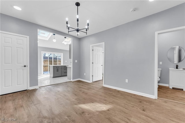 unfurnished dining area featuring a notable chandelier, light wood-type flooring, a skylight, and baseboards