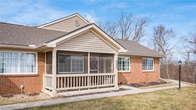 view of front of home featuring a front yard, a sunroom, brick siding, and roof with shingles