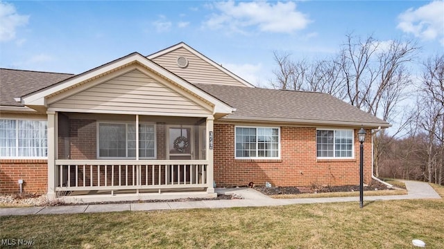 view of front of property with roof with shingles, brick siding, a front lawn, and a porch