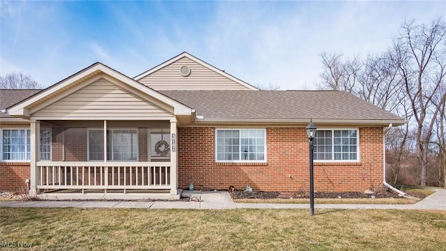 view of front facade featuring brick siding, a front lawn, and a shingled roof