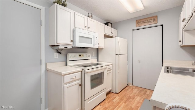 kitchen with light countertops, white appliances, a sink, and white cabinetry