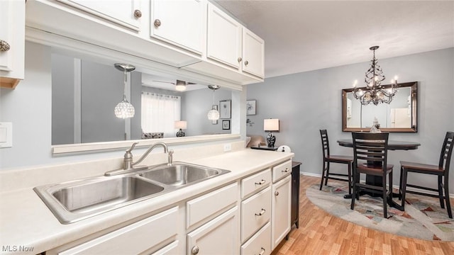 kitchen with light wood finished floors, white cabinets, hanging light fixtures, light countertops, and a sink