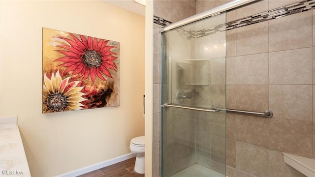 full bathroom with tiled shower, wood finished floors, toilet, and baseboards