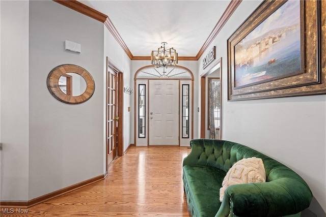 foyer featuring light wood finished floors, baseboards, an inviting chandelier, and ornamental molding