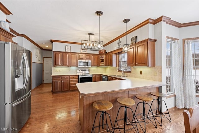 kitchen with brown cabinetry, a breakfast bar area, appliances with stainless steel finishes, light countertops, and a sink