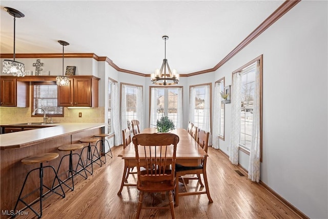 dining space featuring light wood-type flooring, crown molding, baseboards, and a notable chandelier