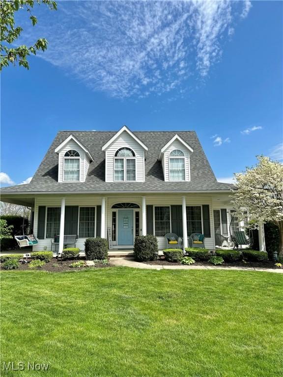 new england style home featuring a porch, a shingled roof, and a front lawn