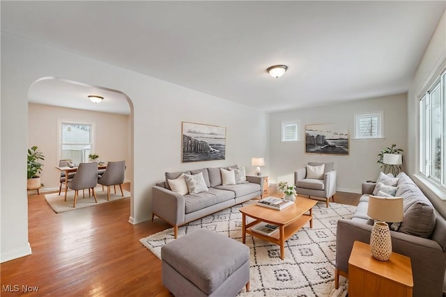 living room featuring arched walkways, baseboards, plenty of natural light, and light wood finished floors