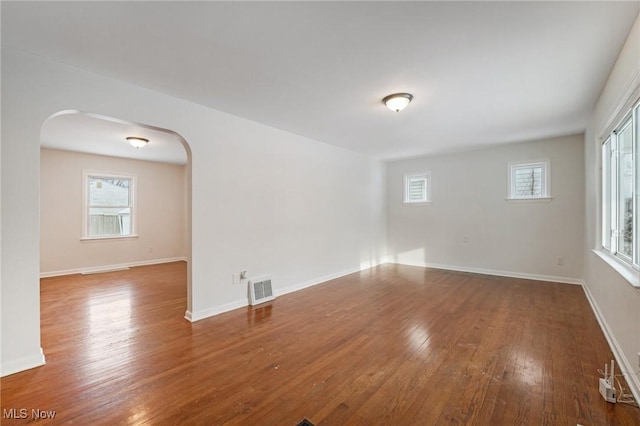 unfurnished room featuring arched walkways, visible vents, baseboards, and wood finished floors