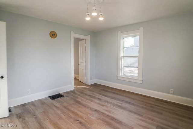 spare room with wood finished floors, visible vents, and baseboards