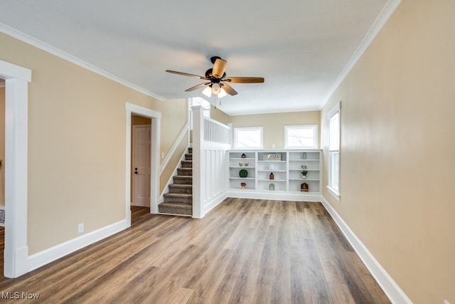 empty room featuring light wood-type flooring, crown molding, stairway, and baseboards