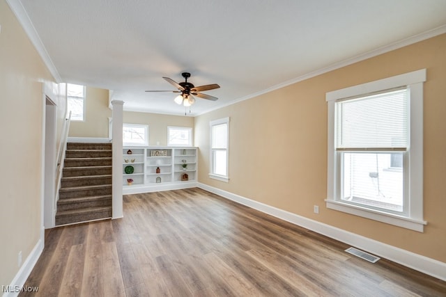 empty room featuring baseboards, visible vents, wood finished floors, and ornamental molding