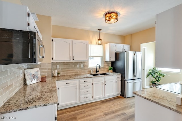 kitchen with white cabinetry, stainless steel appliances, a sink, and decorative light fixtures