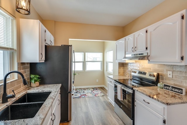 kitchen with light stone counters, appliances with stainless steel finishes, white cabinets, a sink, and under cabinet range hood