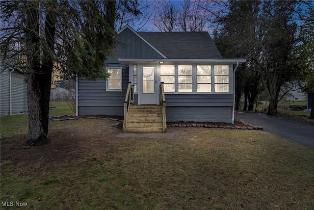 view of front of house featuring entry steps, aphalt driveway, a front yard, and a sunroom