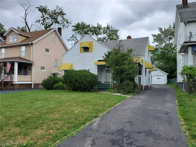 view of front of property featuring driveway, a detached garage, a front lawn, and an outbuilding