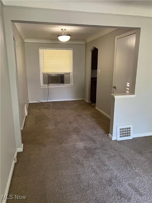 unfurnished room featuring arched walkways, dark colored carpet, visible vents, and baseboards