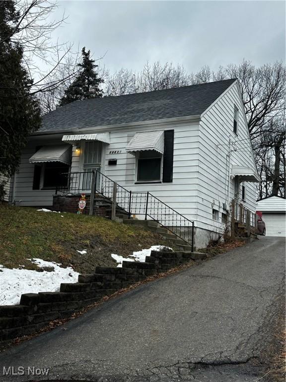 view of front facade with a shingled roof, an outdoor structure, and a detached garage