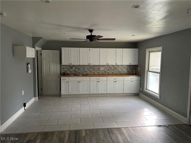 kitchen with decorative backsplash, white cabinetry, wooden counters, and a sink